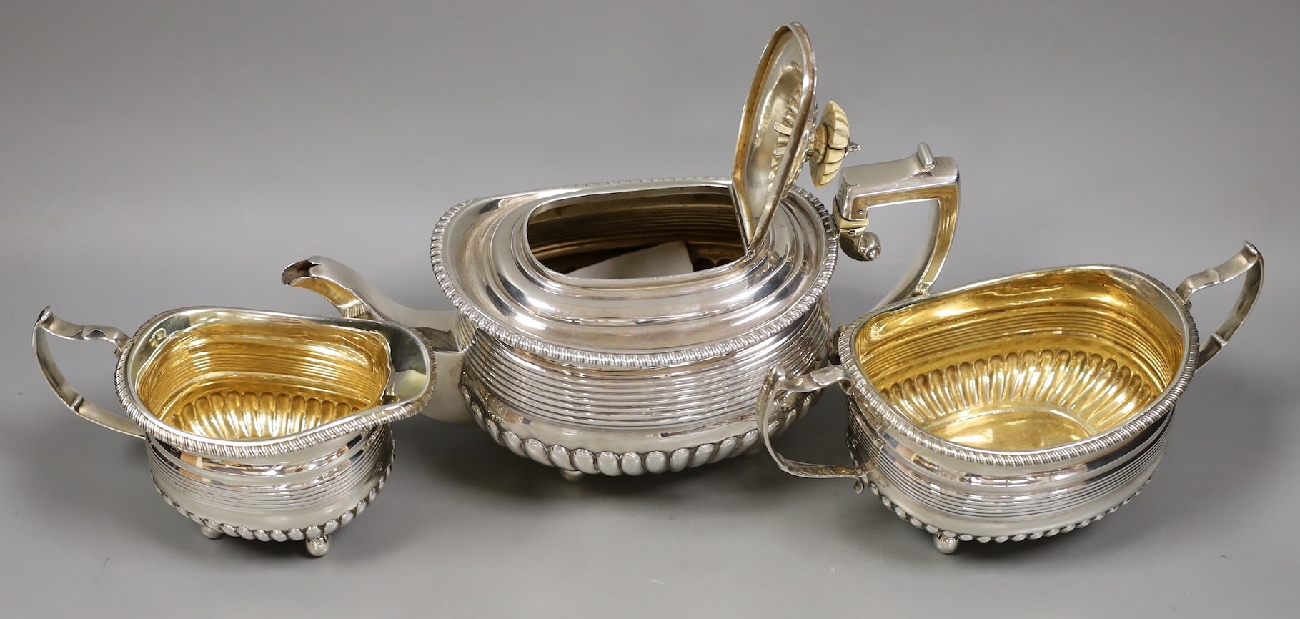 A matched George III demi fluted and reeded silver three piece tea set by Alice & George Burroughs and Walter Bennett (teapot patched), London, 1813, with ivory knop and insulators